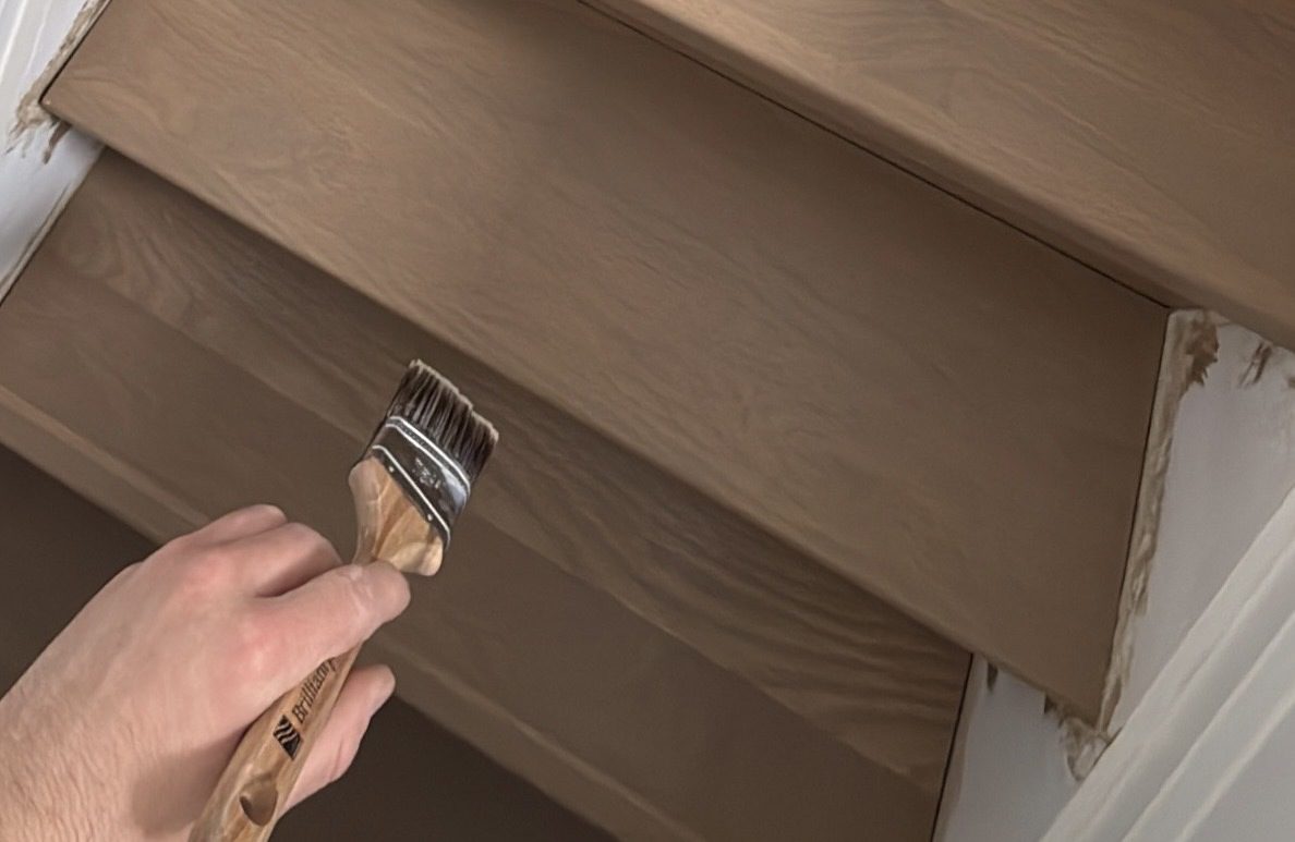 Person applying wood stain to a wooden surface with a brush.