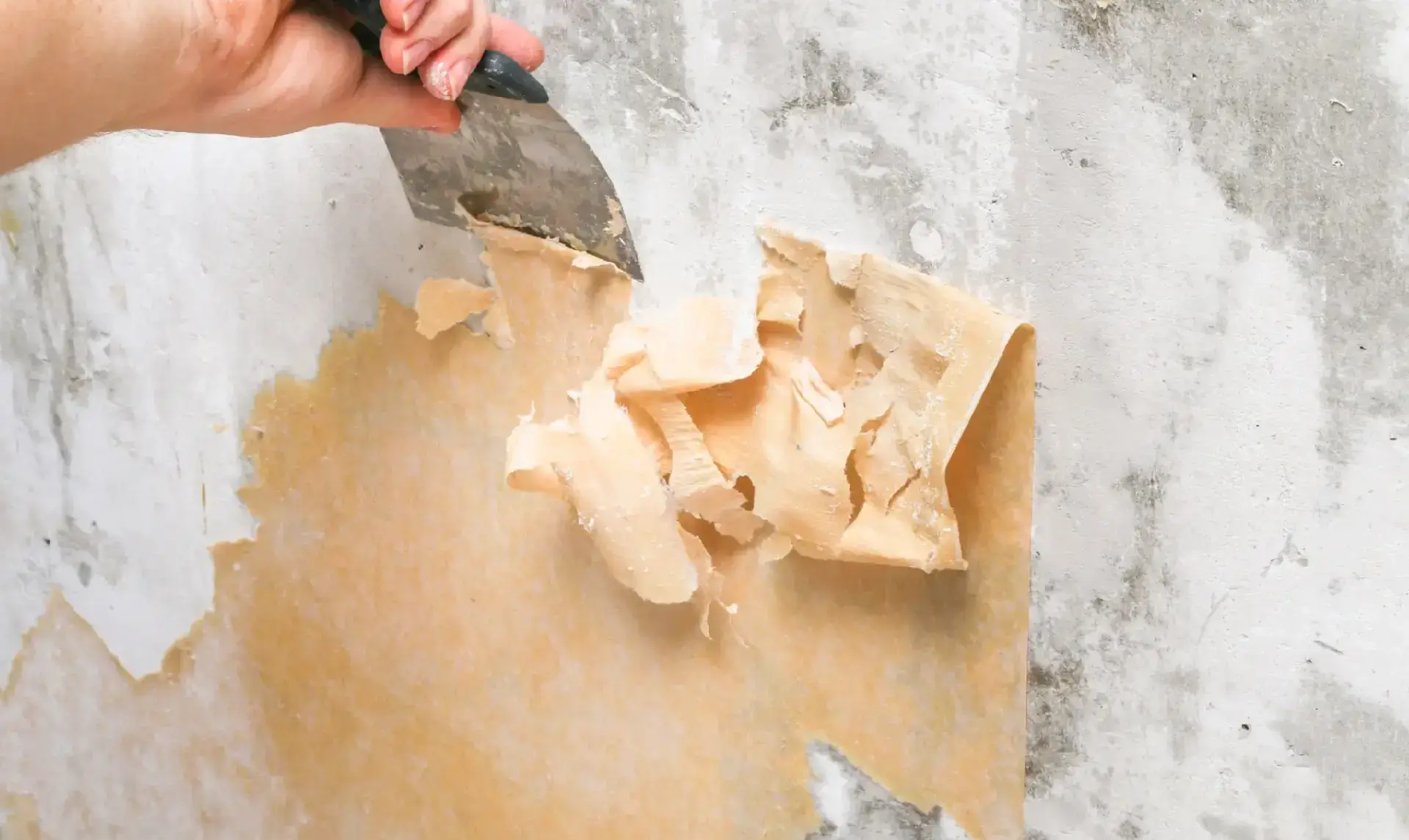 Hand peeling off old wallpaper from a wall.