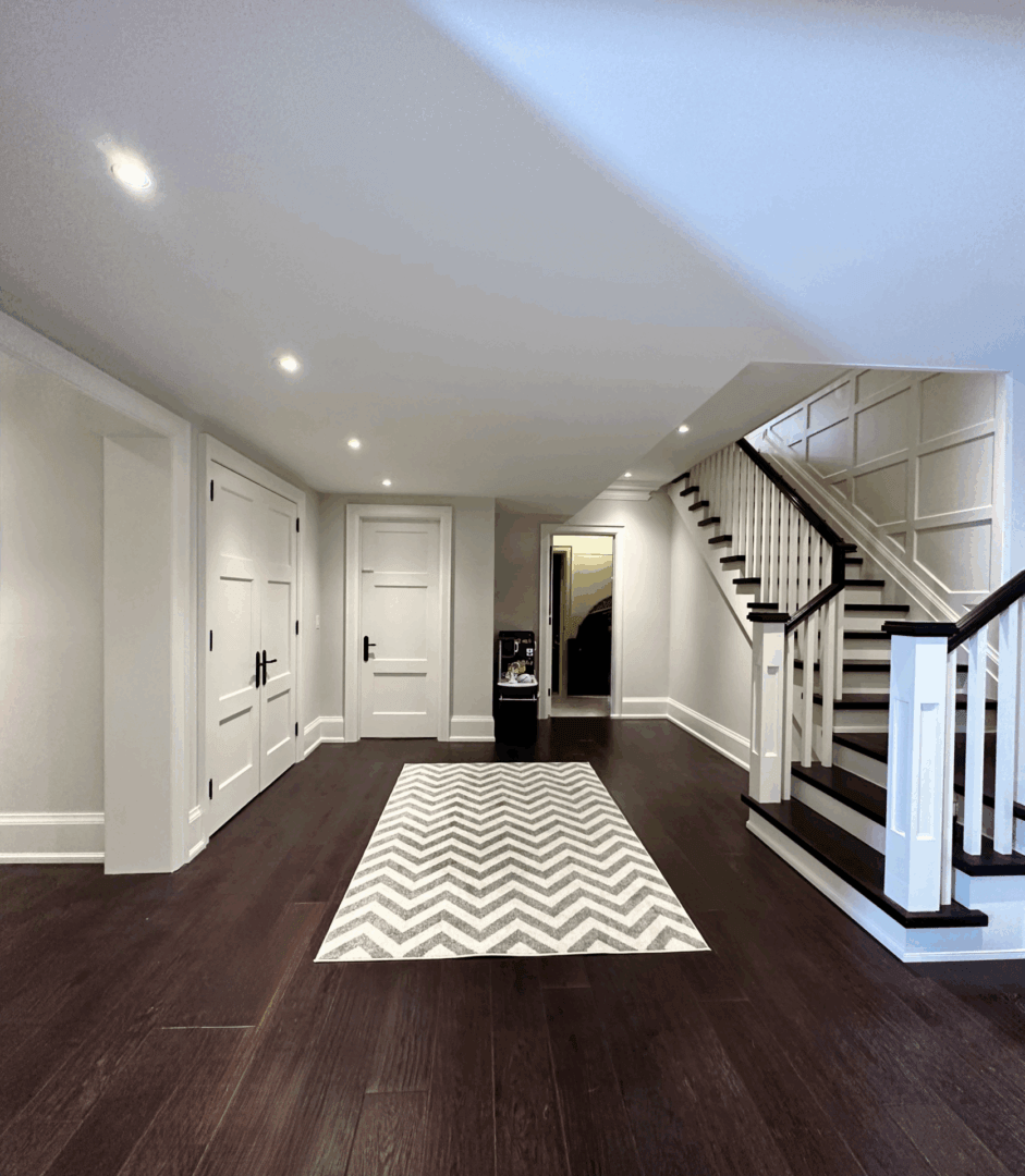 Modern basement with white walls, dark wood floors, and a staircase.