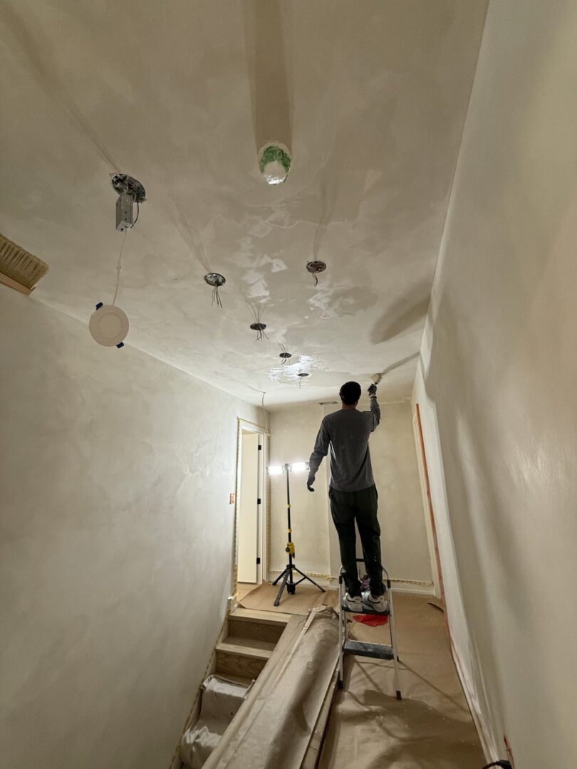 Worker installs ceiling lights in a hallway under renovation.