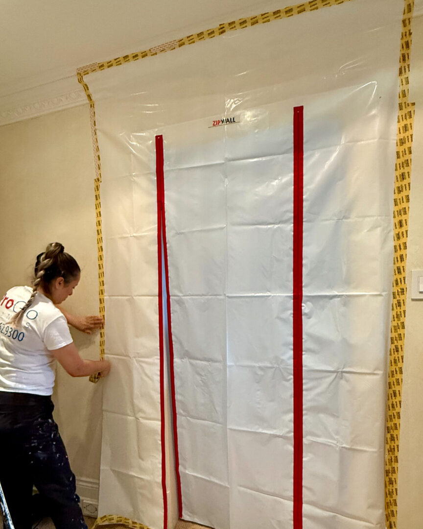 Person applying white adhesive sheet with red stripes on a wall.