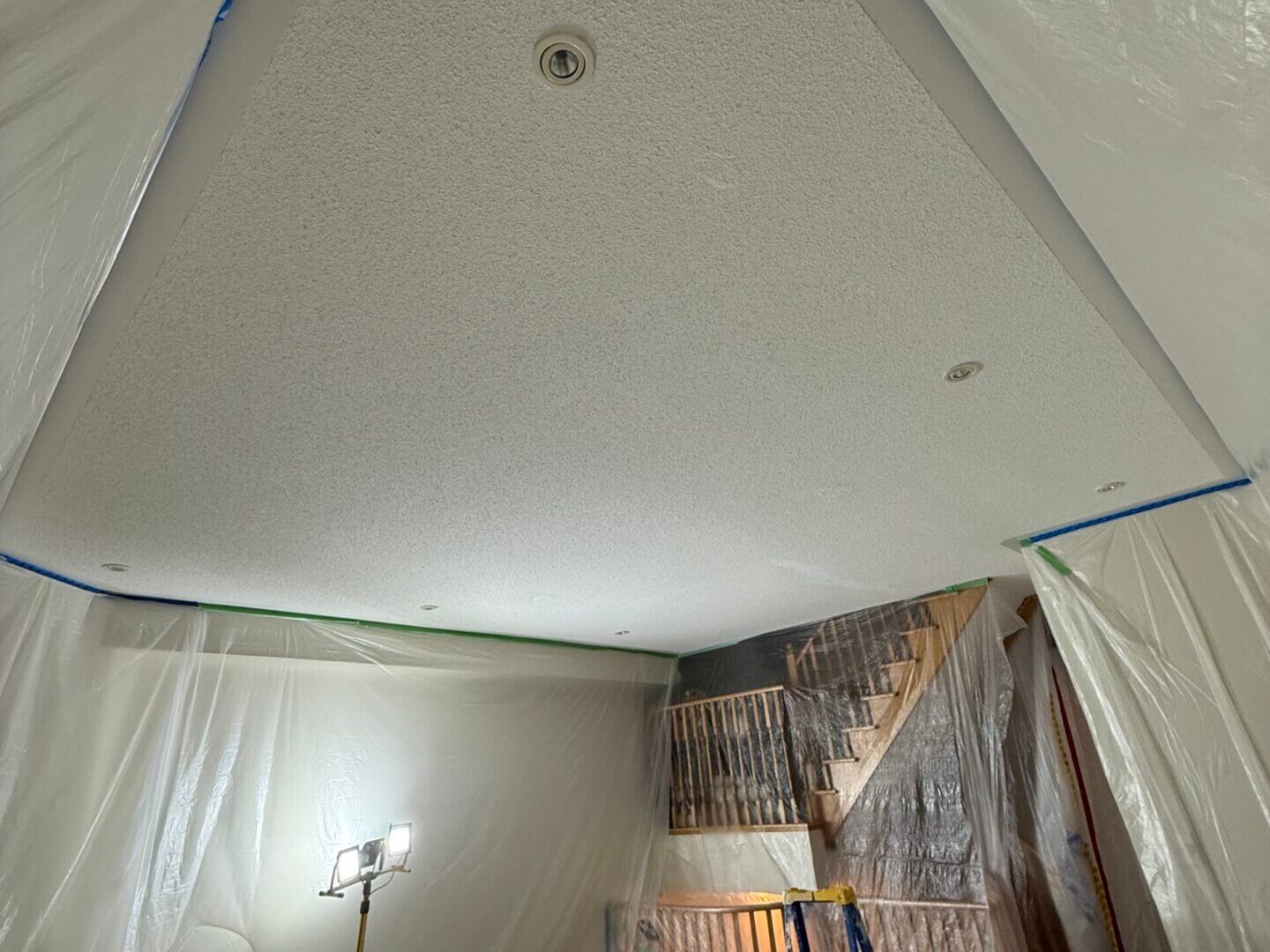 Room under renovation with ceiling work in progress and furniture covered.