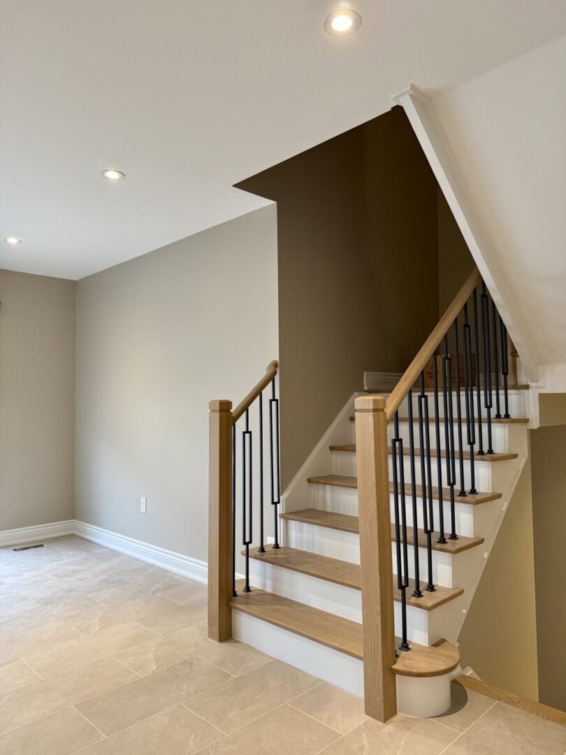 Modern staircase with wooden handrails and metal balusters in a neutral-toned room.