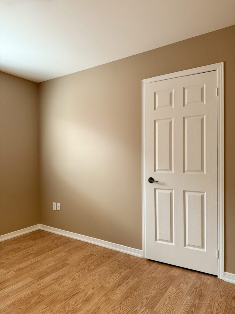 Empty beige room with wooden floor and white door.