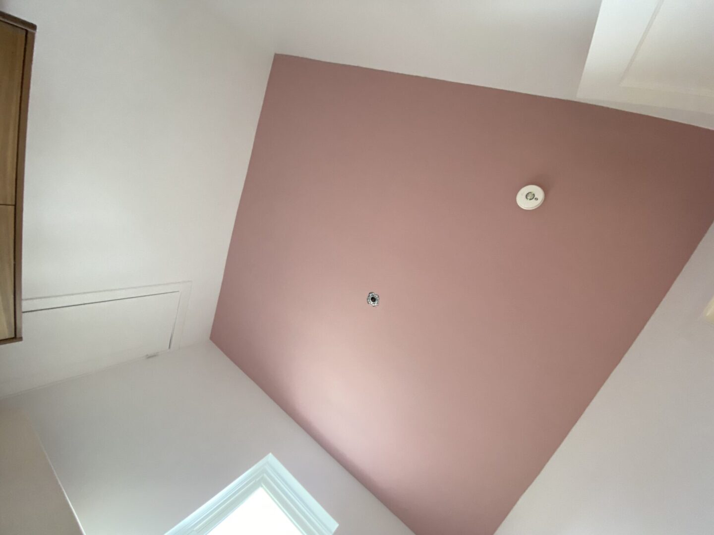 View of a ceiling with pink and white sections and a smoke detector.